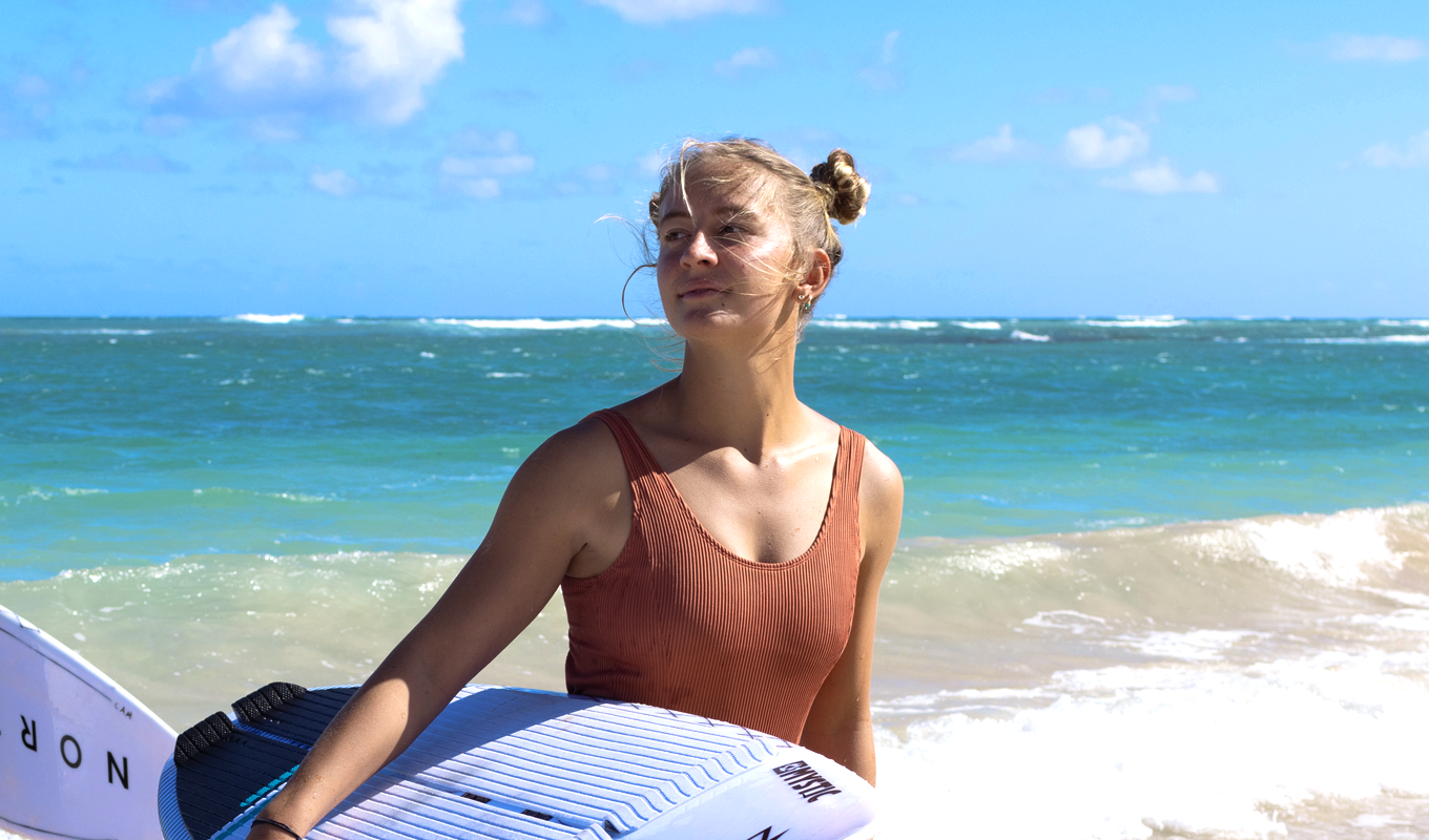 Camille Delannoy sujetando una tabla de surf junto al mar